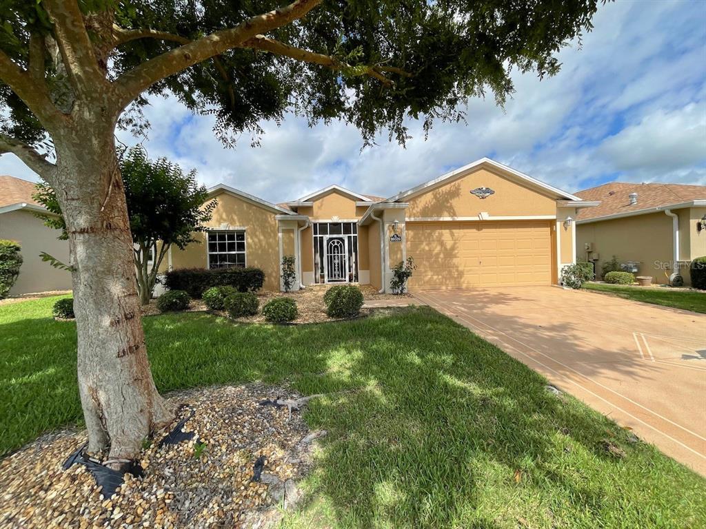 A single-story tan stucco house with a two-car garage and a landscaped front yard — 16026 SW 14TH AVENUE ROAD, OCALA, FL