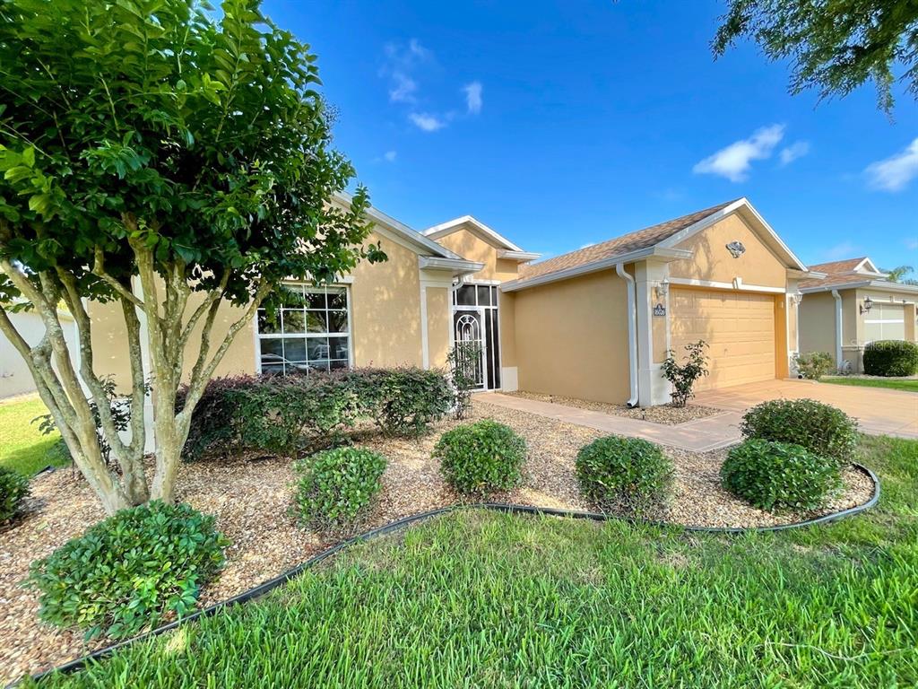 A single-story house with a tan stucco exterior, a two-car garage, and landscaped front yard — 16026 SW 14TH AVENUE ROAD, OCALA, FL