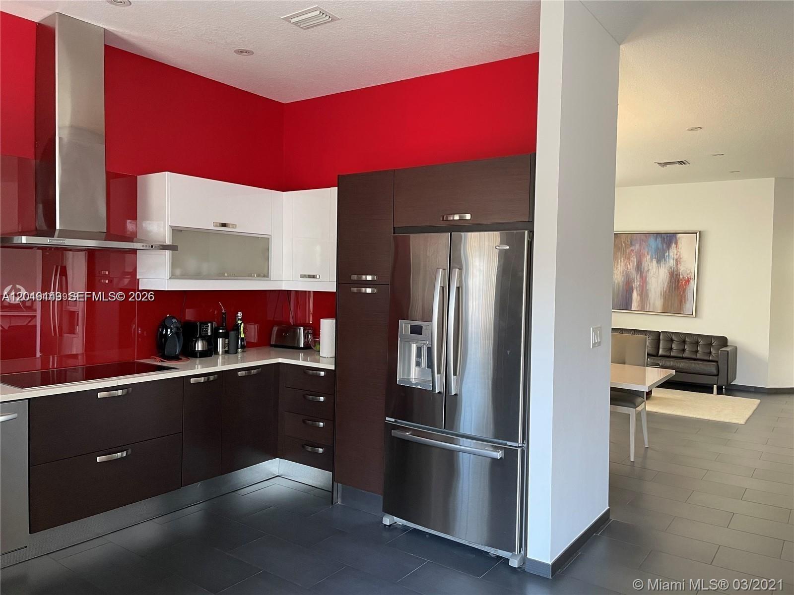 A modern kitchen features dark brown cabinets, white upper cabinets, and a vibrant red backsplash — 10933 NW 73 TE, Doral FL 33178, DORAL, FL