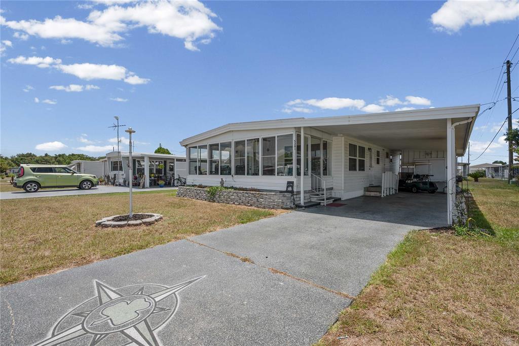 A single-story manufactured home with a screened-in porch, carport, and a compass design on the driveway — 5301 FLINT STREET, ZEPHYRHILLS, FL