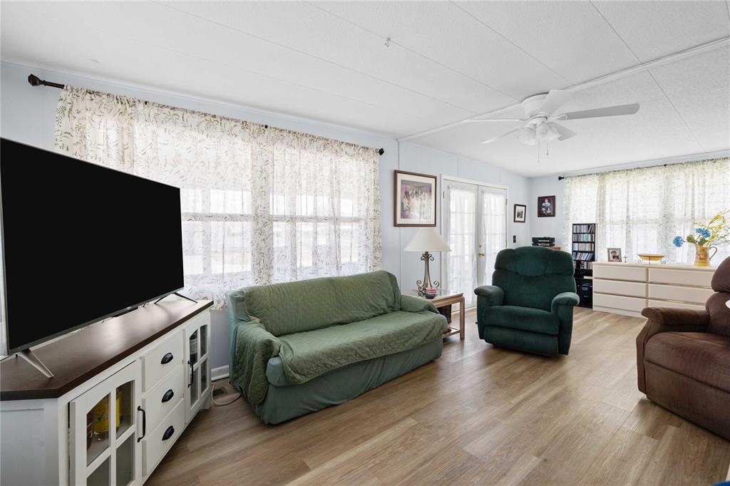 A living room features light wood-look flooring, a green sofa, two recliners, and large windows — 5301 FLINT STREET, ZEPHYRHILLS, FL