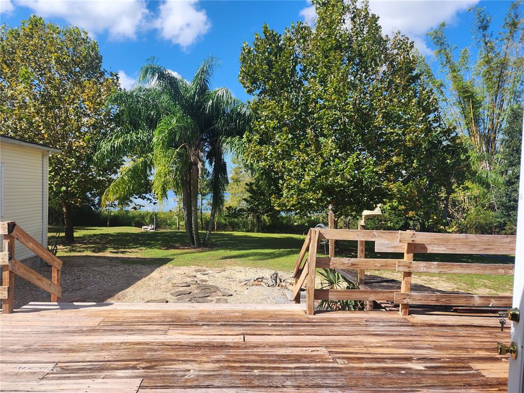 A wooden deck overlooks a grassy backyard with trees, a palm tree, and a lake — 14902 ARRENA ROAD, WINTER GARDEN, FL