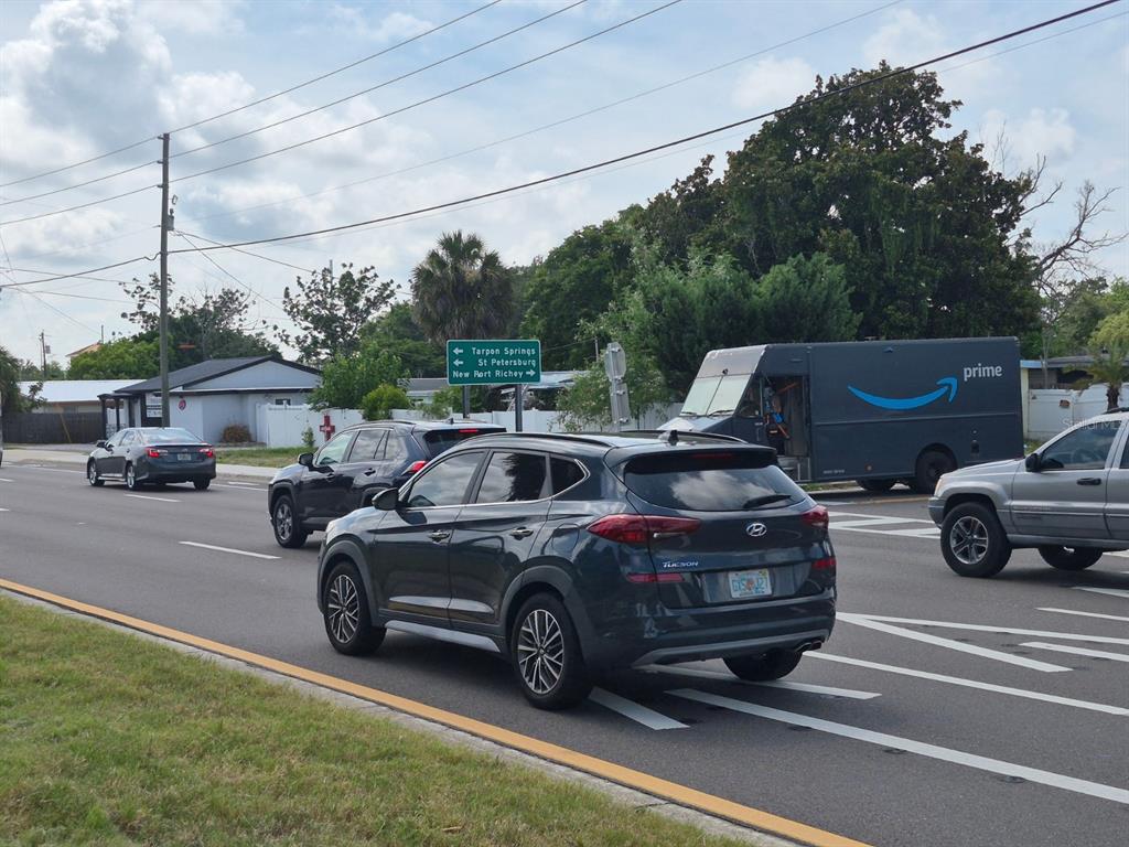 A dark SUV drives on a multi-lane road past an Amazon delivery truck and signage — 4007 FLAMINGO DRIVE, NEW PORT RICHEY, FL