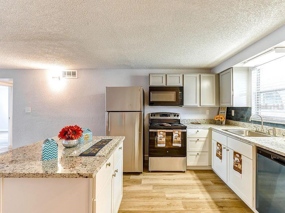A kitchen features white cabinets, granite countertops, stainless steel appliances, and a central island — 9911 AQUARIUS DRIVE UNIT 7, PORT RICHEY, FL