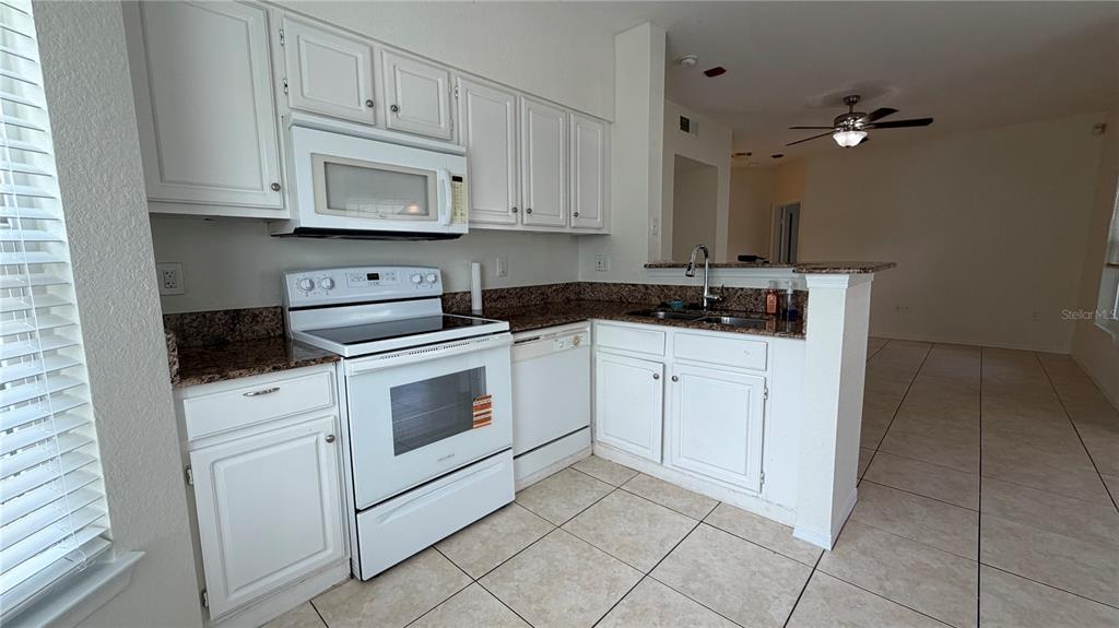 A kitchen features white cabinets, granite countertops, white appliances, and light-colored tile flooring — 23500 WALDEN CENTER DRIVE UNIT 210, ESTERO, FL