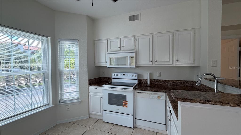 A kitchen features white cabinets, white appliances, granite countertops, and tile flooring — 23500 WALDEN CENTER DRIVE UNIT 210, ESTERO, FL