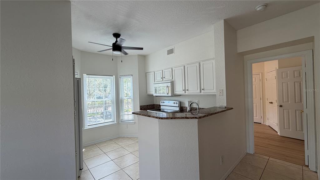 A kitchen features white cabinets, granite countertops, a breakfast bar, and a dining nook — 23500 WALDEN CENTER DRIVE UNIT 210, ESTERO, FL