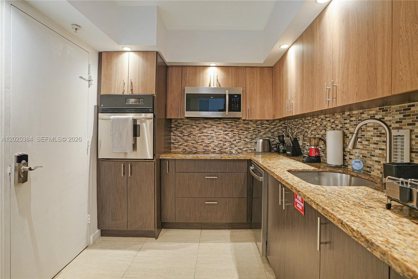 A kitchen features wood-tone cabinets, granite countertops, stainless steel appliances, and a mosaic tile backsplash — 4001 S Ocean Dr # 3P, Hollywood FL 33019, HOLLYWOOD, FL