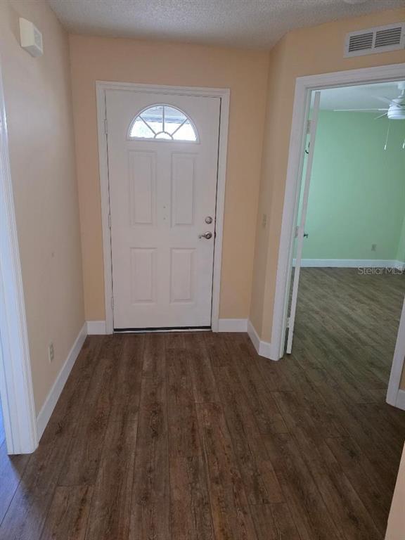 An entryway with wood-look flooring leads to a white front door and an adjacent room — 9028 SW 91ST CIRCLE, OCALA, FL