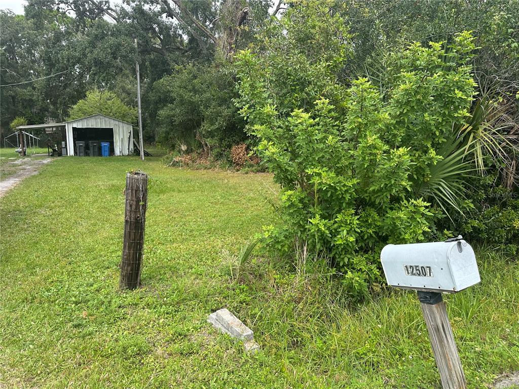 A grassy lot features a metal shed, a wooden fence post, and a mailbox — 12507 GLENNA AVENUE, TAMPA, FL