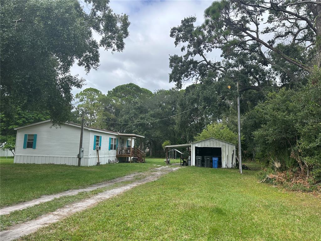 A white mobile home with a detached carport sits on a grassy lot with trees — 12507 GLENNA AVENUE, TAMPA, FL