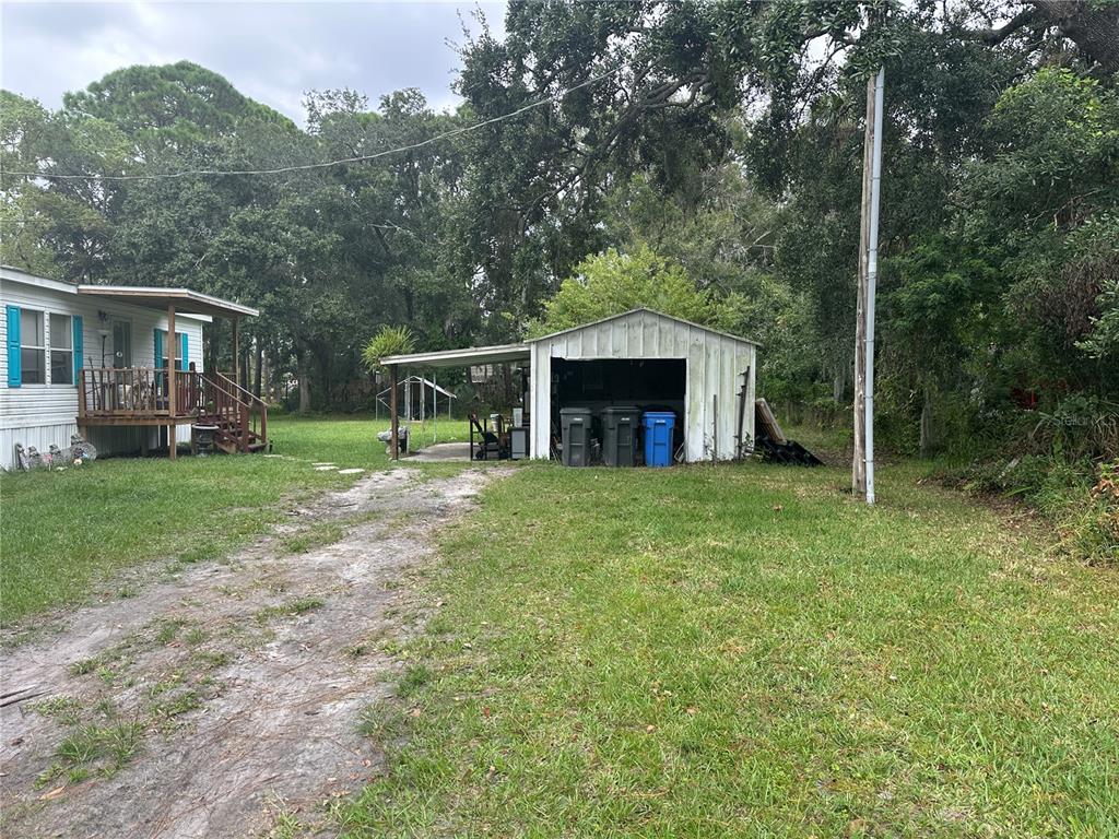 A mobile home with a wooden porch sits next to a detached metal storage shed — 12507 GLENNA AVENUE, TAMPA, FL