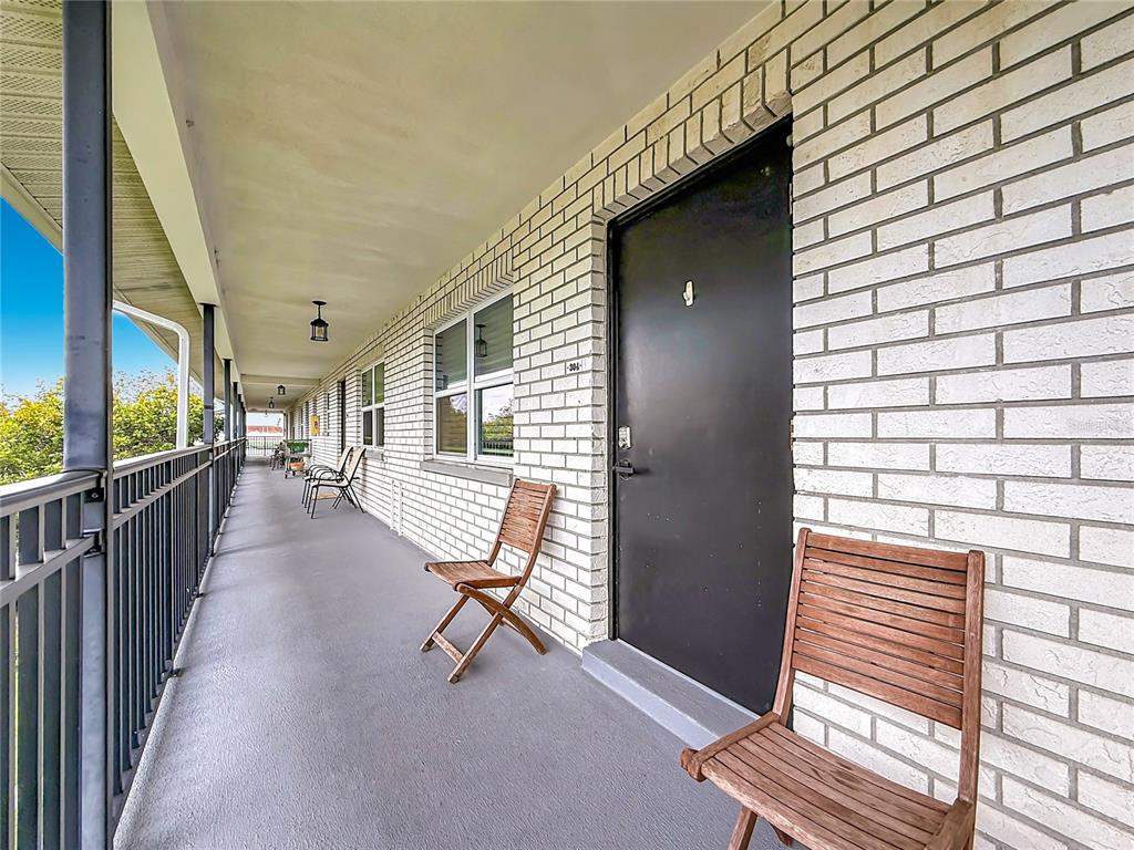 A covered outdoor walkway features white brick walls, a black door, and wooden chairs — 4050 4TH STREET N UNIT 304, ST PETERSBURG, FL