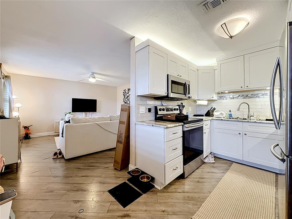 A kitchen with white cabinets and stainless steel appliances opens into a living room area — 4050 4TH STREET N UNIT 304, ST PETERSBURG, FL