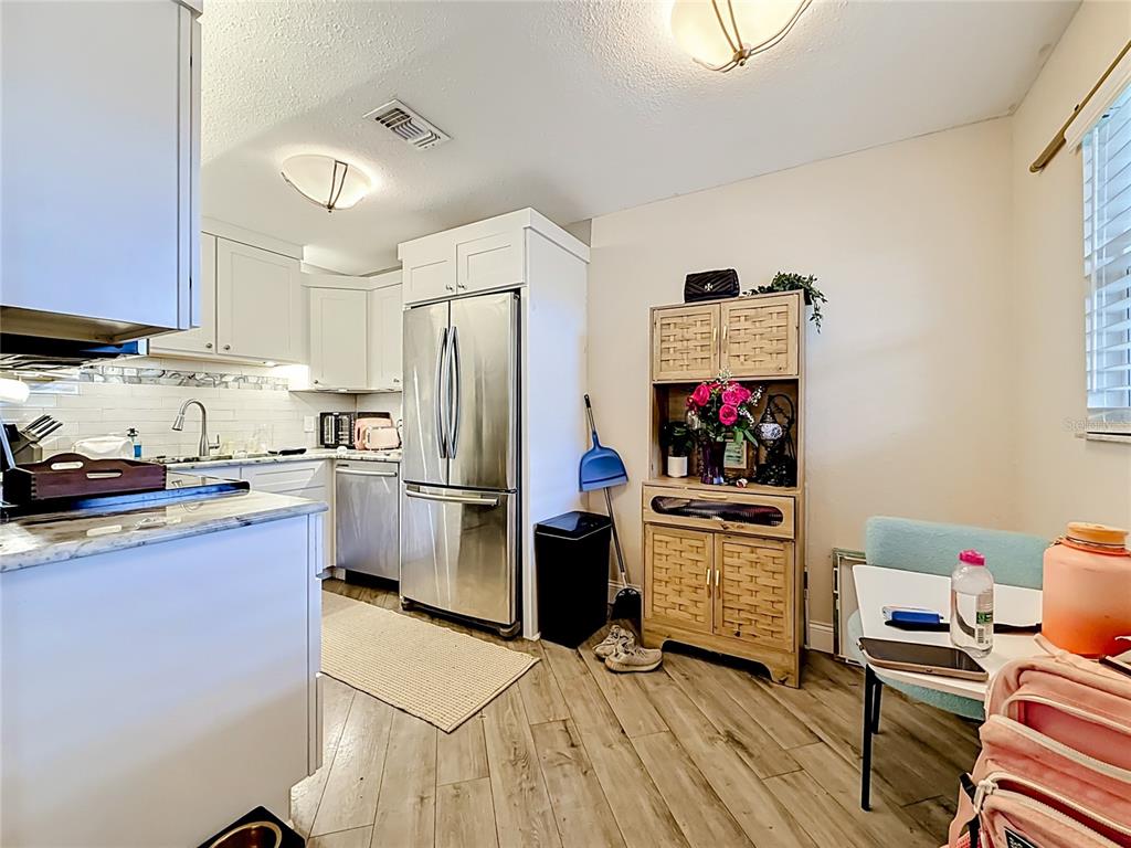 A kitchen features white cabinets, stainless steel appliances, wood-look flooring, and a dining area — 4050 4TH STREET N UNIT 304, ST PETERSBURG, FL