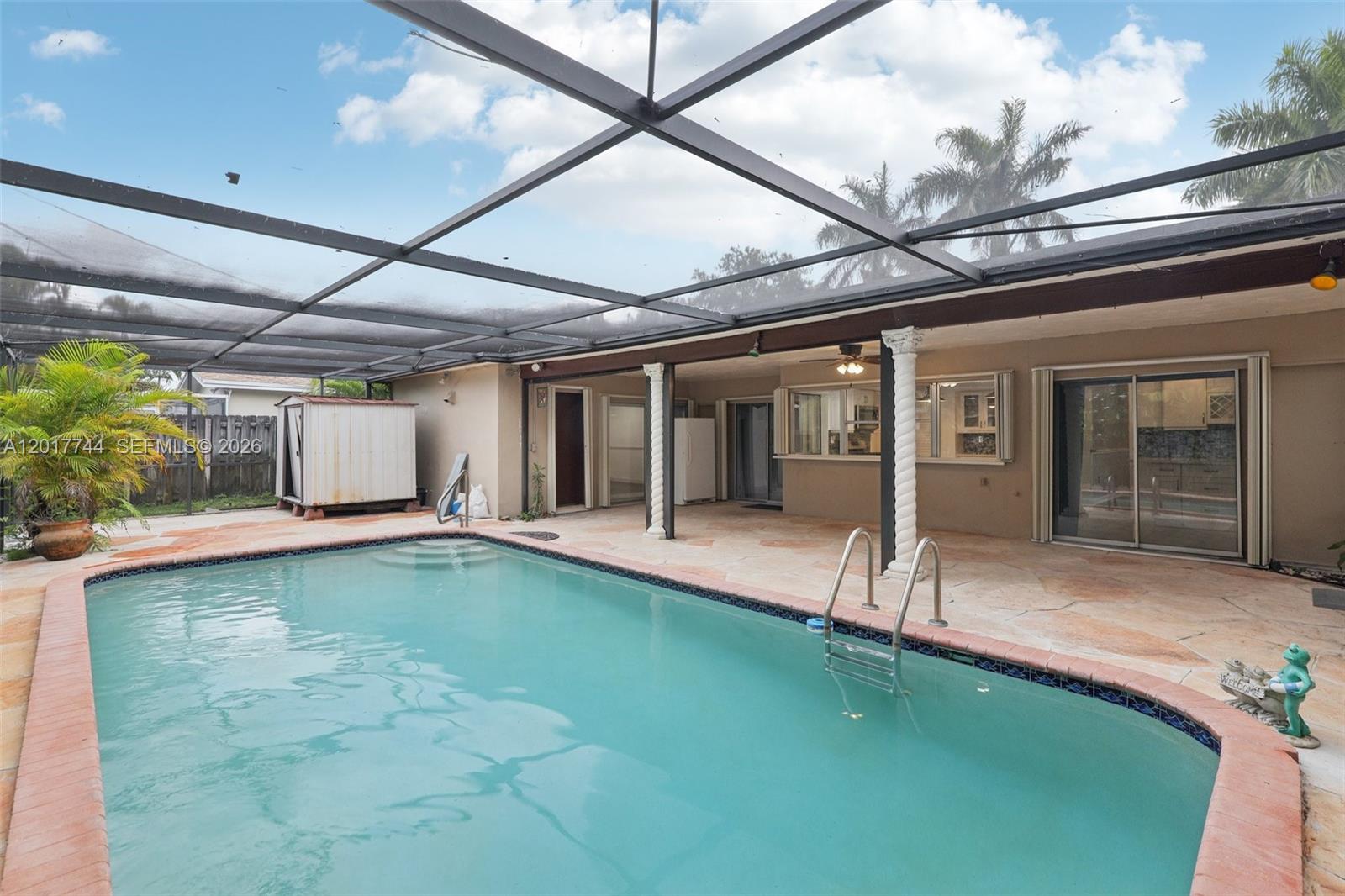 A screened-in patio features a swimming pool, stone decking, and two decorative white columns — 3842 Jasmine Avenue, Miramar FL 33023, MIRAMAR, FL
