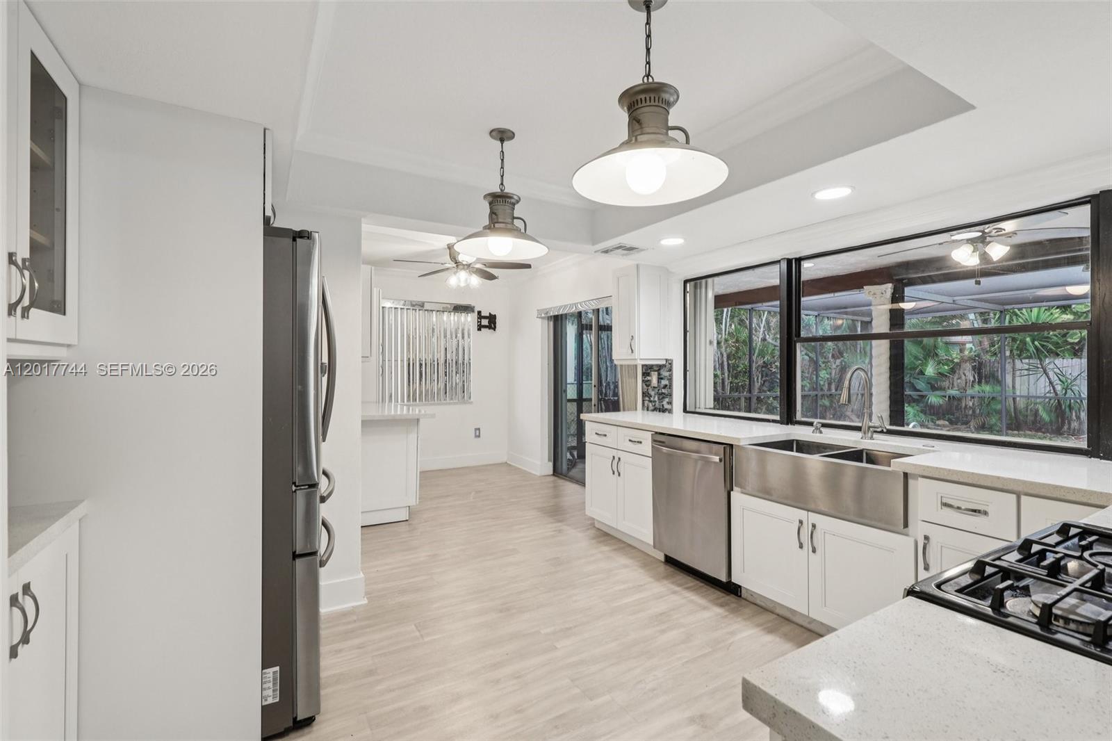 A white kitchen features stainless steel appliances, a farmhouse sink, and two pendant lights — 3842 Jasmine Avenue, Miramar FL 33023, MIRAMAR, FL