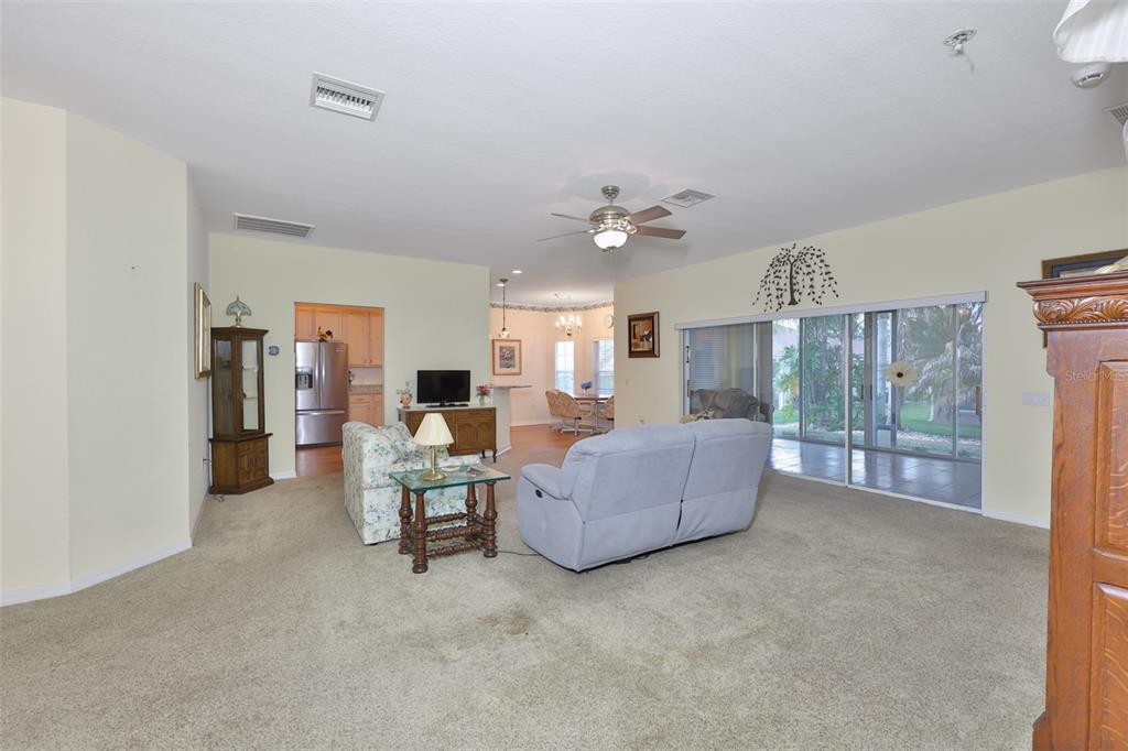 A living room with beige carpet, a ceiling fan, and sliding glass doors to a patio — 4465 STRATHMORE DRIVE, LAKE WALES, FL