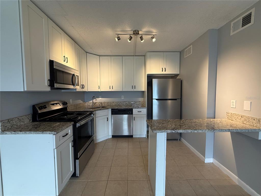 A kitchen features white cabinets, granite countertops, stainless steel appliances, and a breakfast bar — 927 S PINE RIDGE CIRCLE UNIT G2, SANFORD, FL