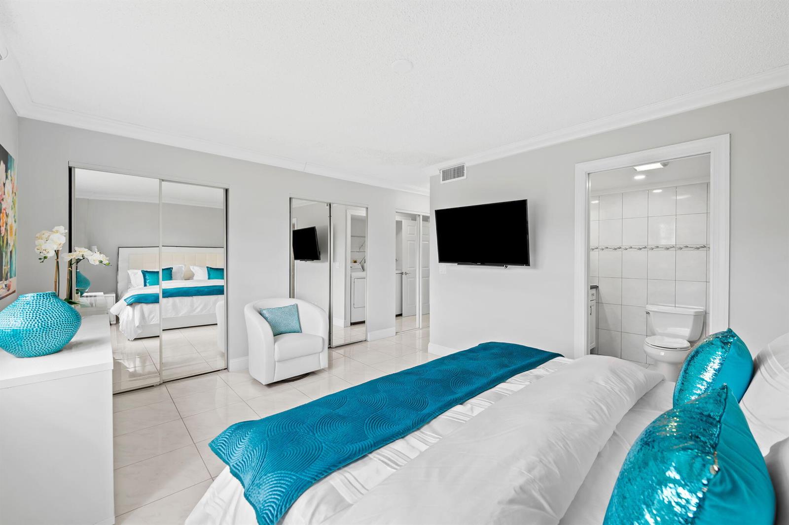 A bedroom features white tile floors, a bed with blue accents, and an attached bathroom — 170 SE 5th Avenue # 103, Dania Beach FL 33004, DANIA BEACH, FL