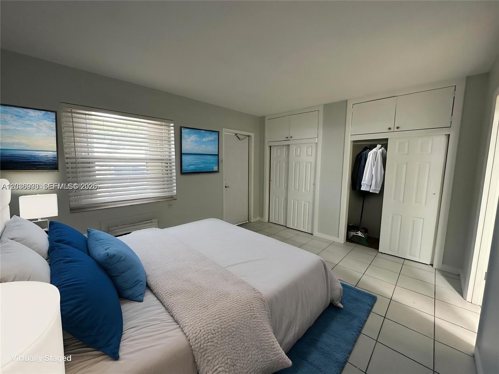 A bedroom features a bed, tiled floors, white closets, and two ocean-themed wall art pieces — 2916 Funston St # 47A, Hollywood FL 33020, HOLLYWOOD, FL