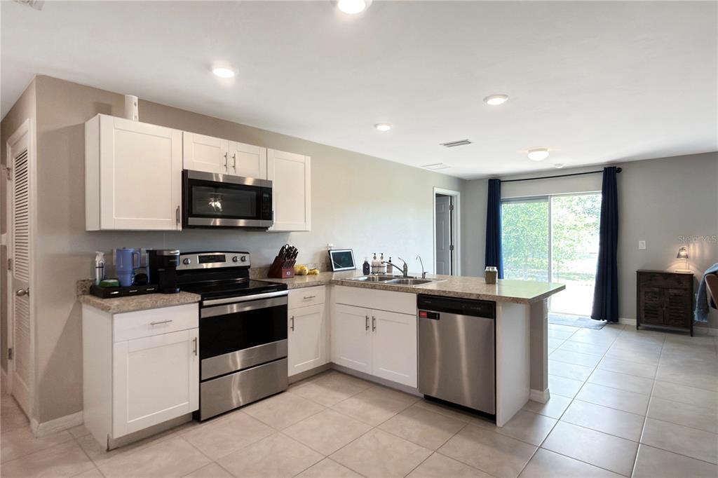 A kitchen features white cabinets, stainless steel appliances, and a peninsula overlooking a dining area — 4323 NE 21ST AVENUE, CAPE CORAL, FL