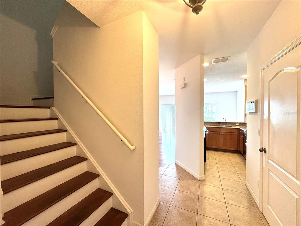 An interior view shows a staircase with wooden treads next to a tiled kitchen area — 10735 SAVANNAH WOOD DRIVE UNIT 208, ORLANDO, FL