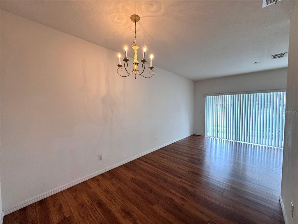 An empty dining room features wood-look flooring, white walls, and a traditional chandelier — 10735 SAVANNAH WOOD DRIVE UNIT 208, ORLANDO, FL