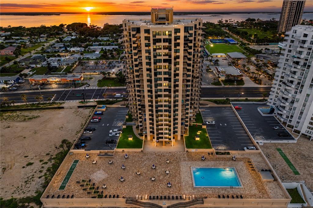 An aerial view shows a tall residential building with a pool deck at sunset — 3051 S ATLANTIC AVENUE UNIT V060, DAYTONA BEACH SHORES, FL