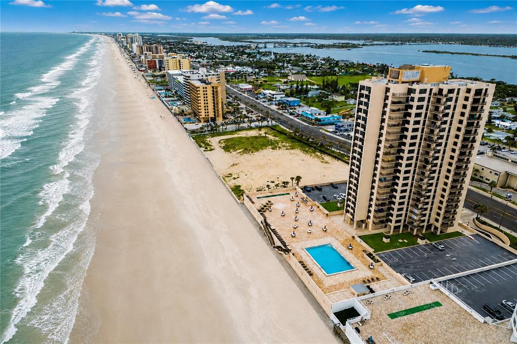 An aerial view shows a high-rise beachfront condominium with a pool deck and parking — 3051 S ATLANTIC AVENUE UNIT V060, DAYTONA BEACH SHORES, FL