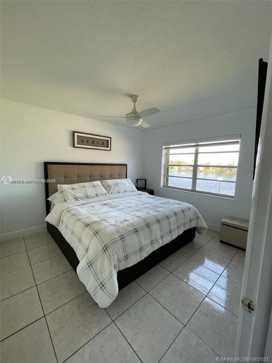 A bedroom features a bed with a plaid comforter, tile flooring, and a waterfront view — 12860 SW 43rd Dr # B, Miami FL 33175, MIAMI, FL