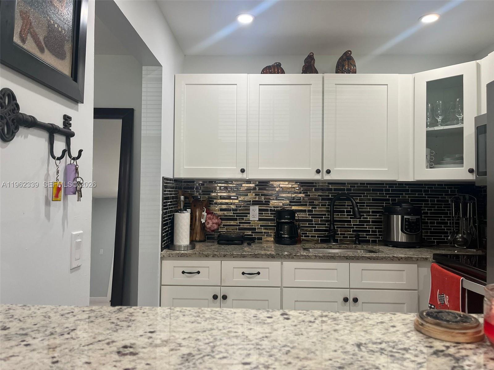 A kitchen features white cabinets, granite countertops, and a dark horizontal tile backsplash — 35 Camden # B, West Palm Beach FL 33417, WEST PALM BEACH, FL