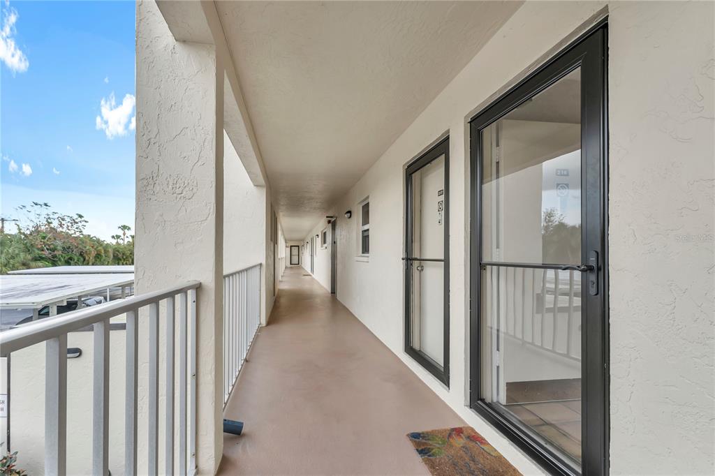 An outdoor apartment building walkway with a metal railing and two glass screen doors — 915 BEACH ROAD UNIT 216, SARASOTA, FL