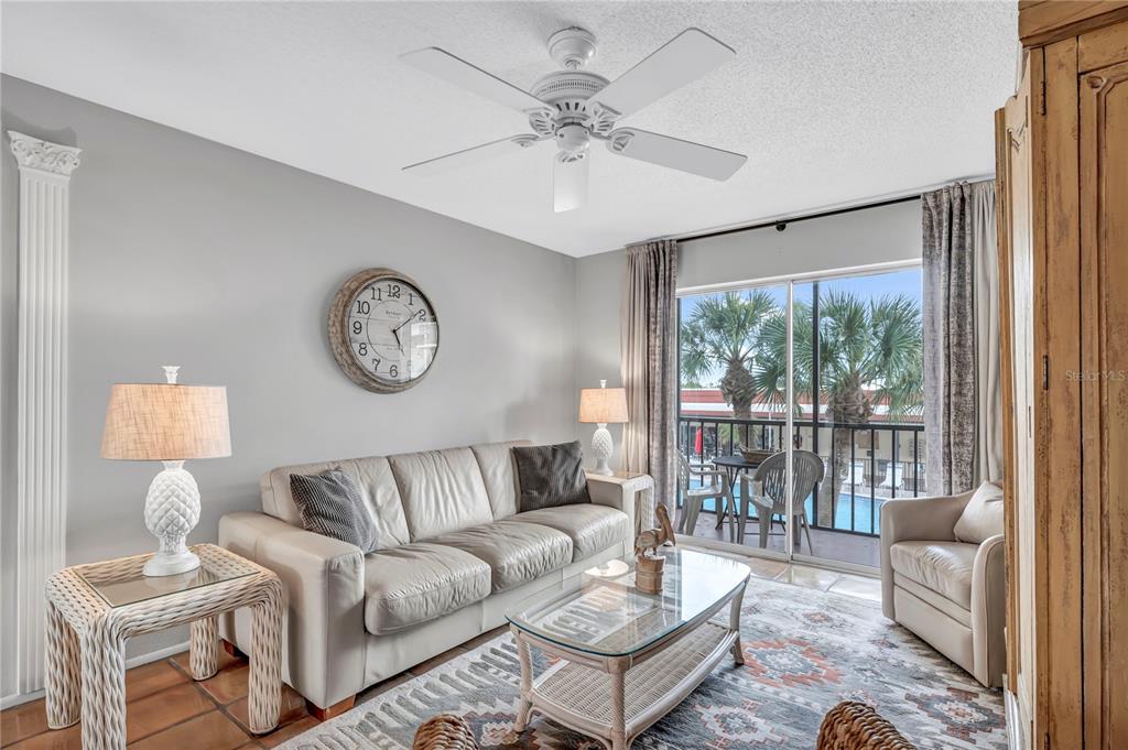 A living room features a beige sofa, glass coffee table, wall clock, and a balcony view — 915 BEACH ROAD UNIT 216, SARASOTA, FL