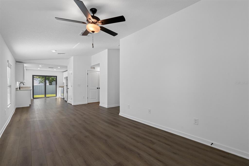 An open-concept living area features wood-look flooring, white walls, and a ceiling fan — 11290 LIBERTO ROAD, WEEKI WACHEE, FL
