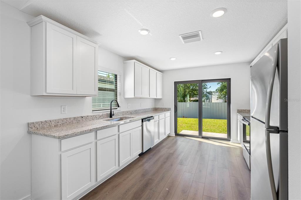 A kitchen features white cabinets, granite countertops, stainless steel appliances, and a sliding glass door — 11290 LIBERTO ROAD, WEEKI WACHEE, FL