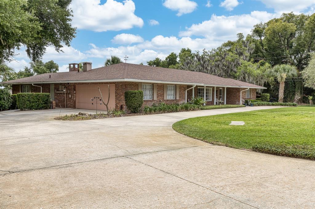 A single-story brick house with a large concrete driveway and a sprawling lawn — 900 N CITRUS AVENUE, HOWEY IN THE HILLS, FL
