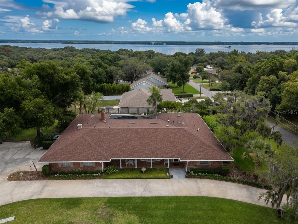An aerial view shows a single-story brick house with a brown shingled roof and driveway — 900 N CITRUS AVENUE, HOWEY IN THE HILLS, FL