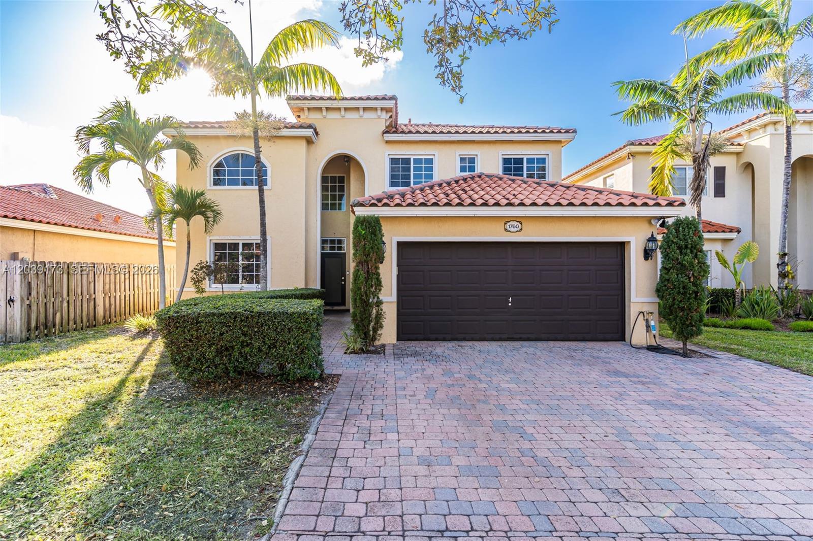 A two-story stucco house features a brown garage door, tiled roof, and palm trees — 1760 NE 36th Ave, Homestead FL 33033, HOMESTEAD, FL