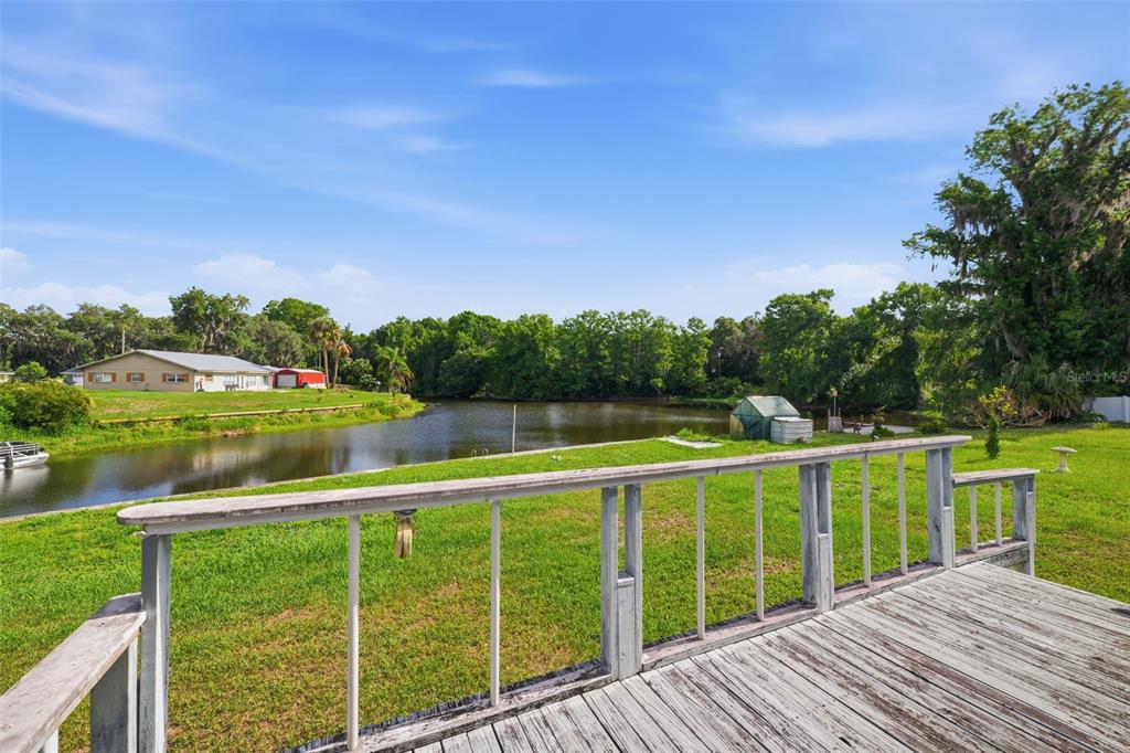 A wooden deck overlooks a grassy lawn, a small pond, and trees under a blue sky — 1830 S MANDARIN TERRACE, INVERNESS, FL