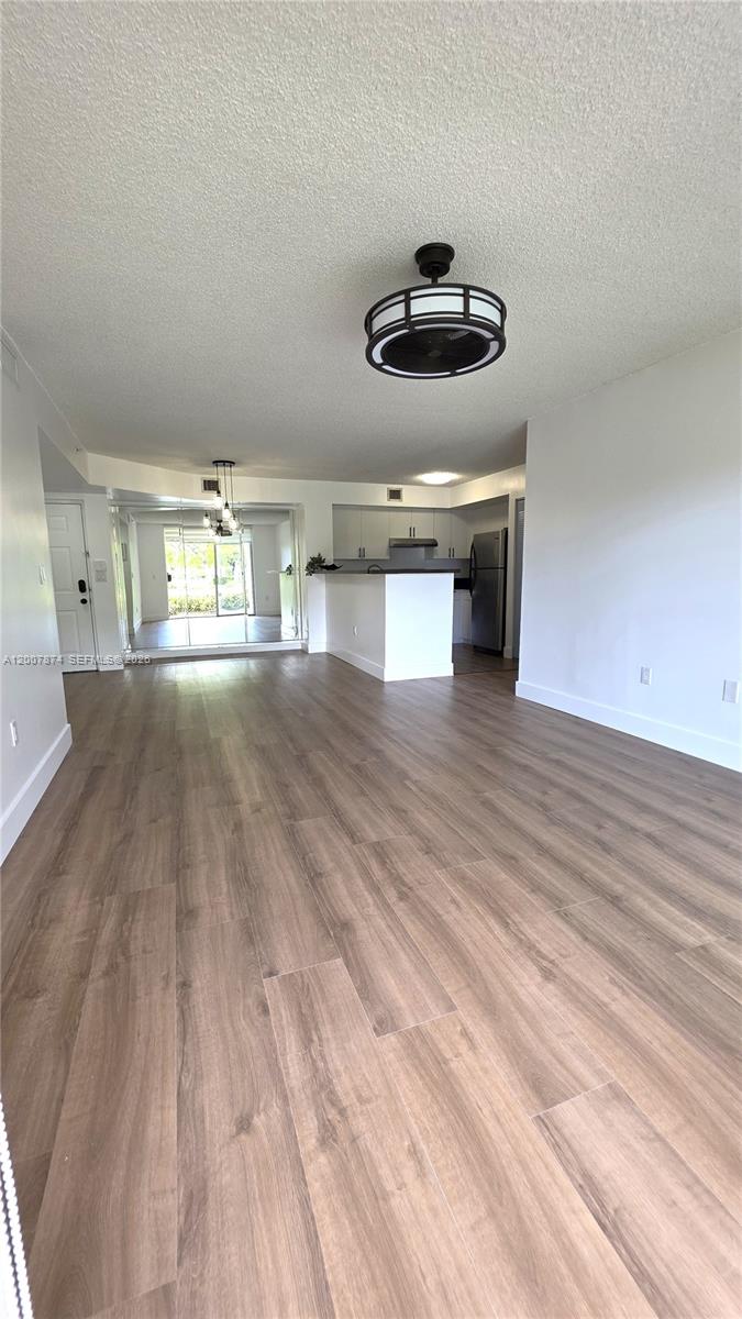 An open-concept living area features light wood-look flooring, a kitchen island, and a mirrored wall — 12136 Saint Andrews Pl # 108, Miramar FL 33025, MIRAMAR, FL