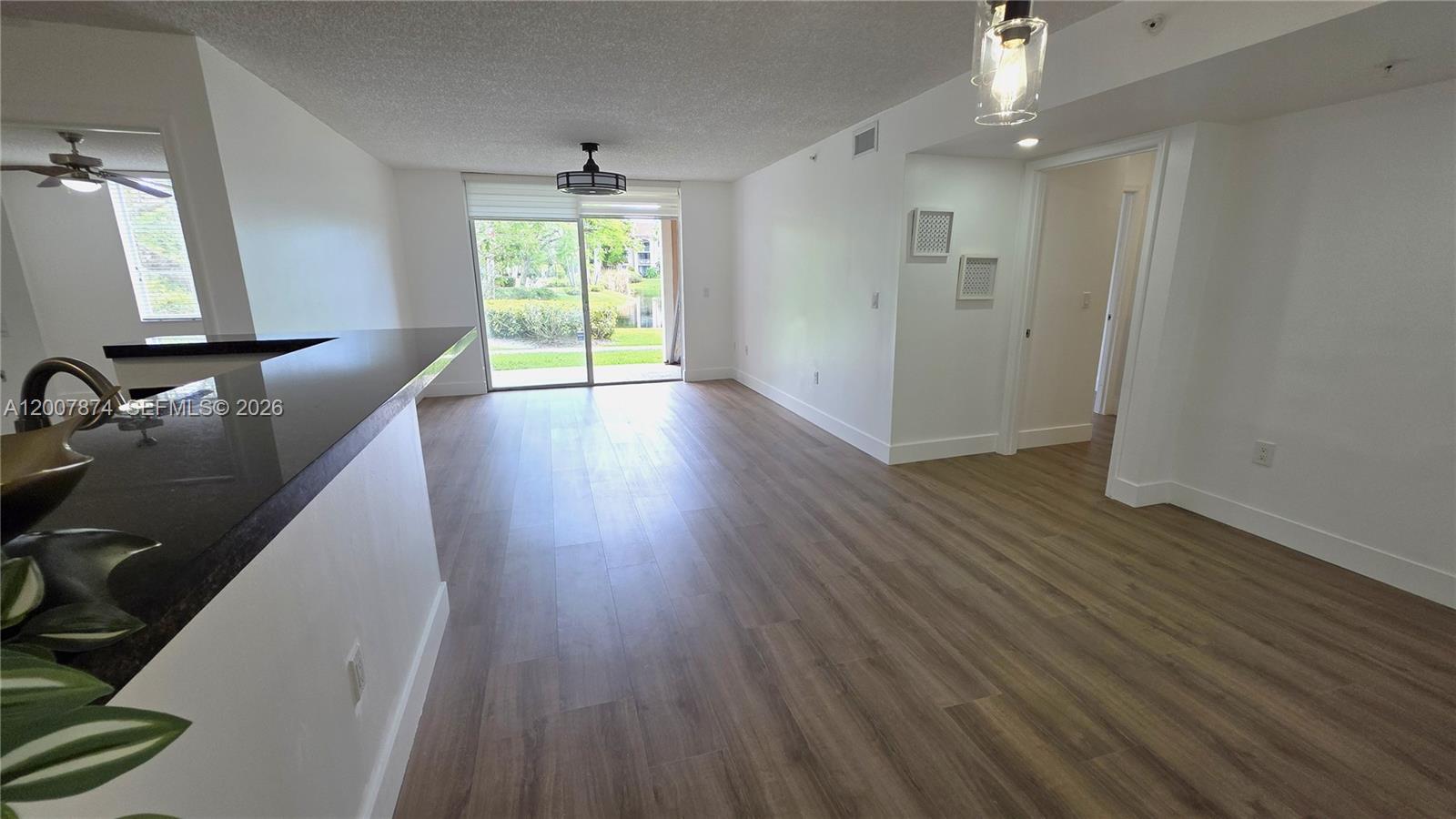 An open-concept living area features wood-look flooring, a kitchen breakfast bar, and sliding glass doors — 12136 Saint Andrews Pl # 108, Miramar FL 33025, MIRAMAR, FL