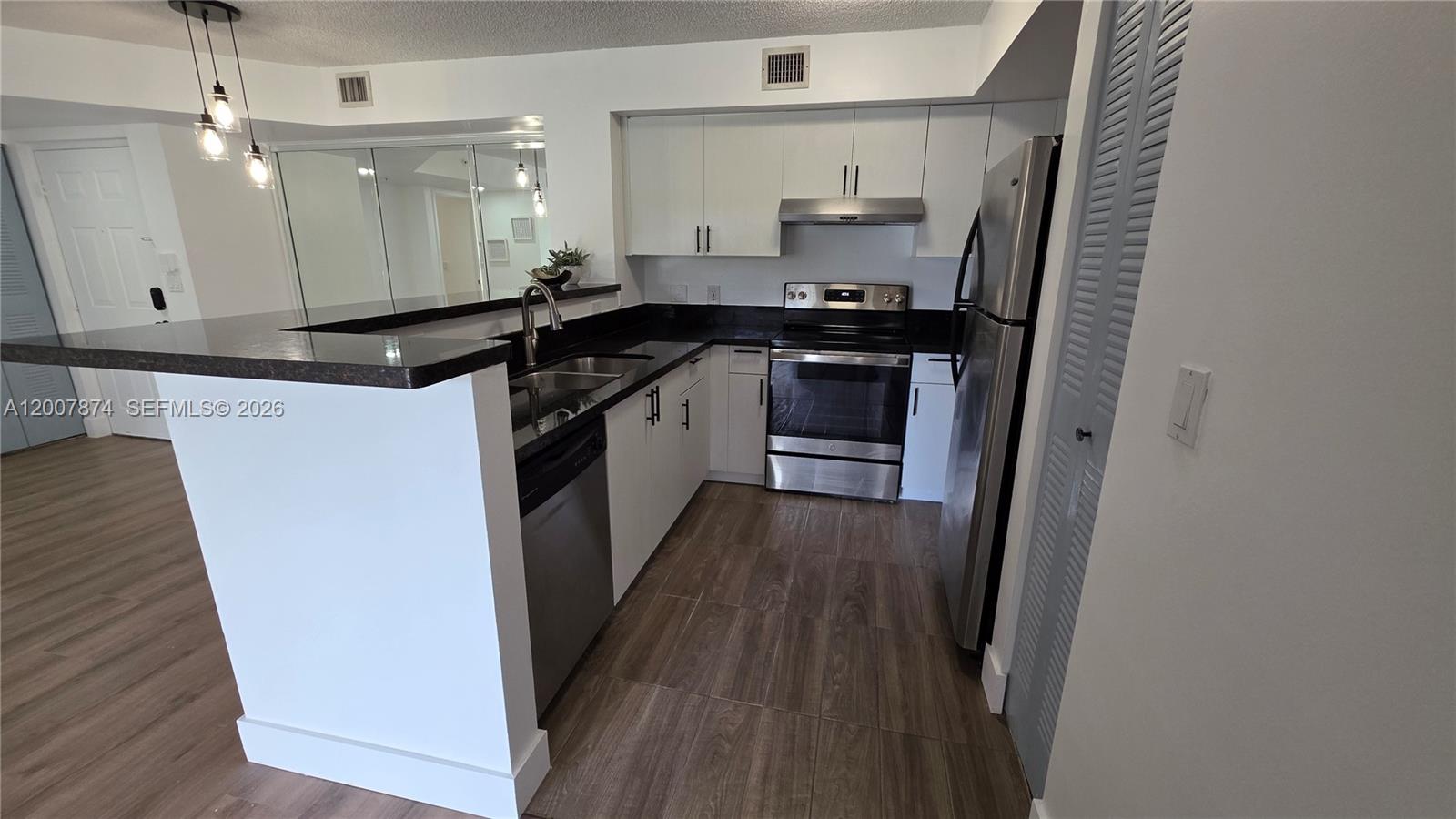 A kitchen features white cabinets, stainless steel appliances, and a dark countertop breakfast bar — 12136 Saint Andrews Pl # 108, Miramar FL 33025, MIRAMAR, FL