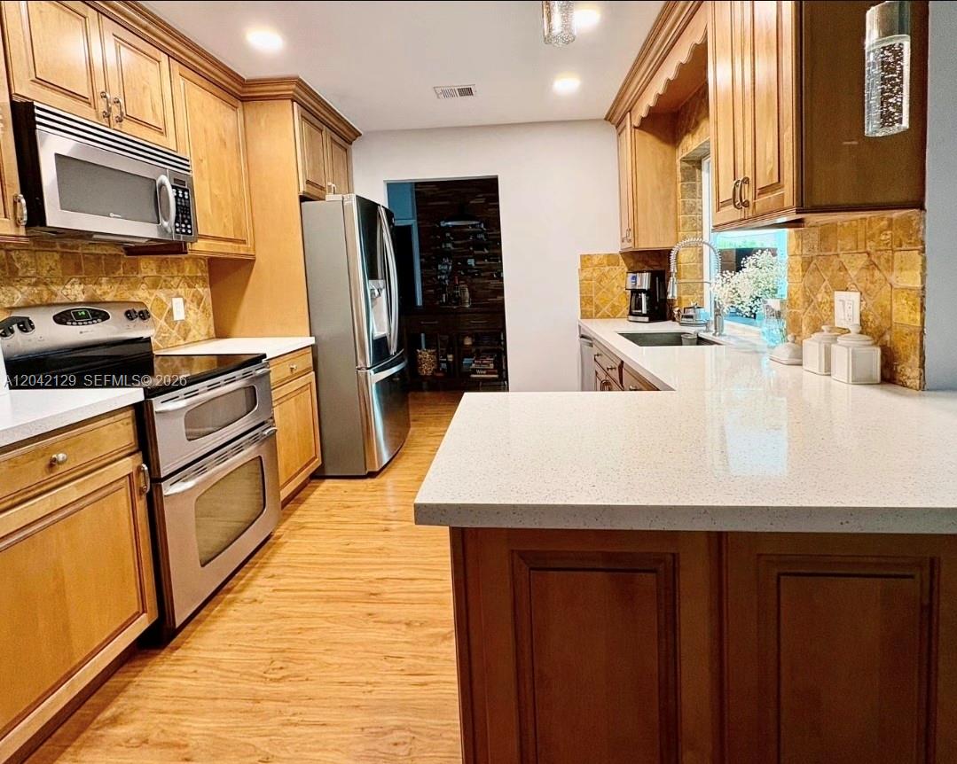 A kitchen features wood cabinets, stainless steel appliances, a white countertop, and a tiled backsplash — 1903 NW 79th Ave, Margate FL 33063, MARGATE, FL