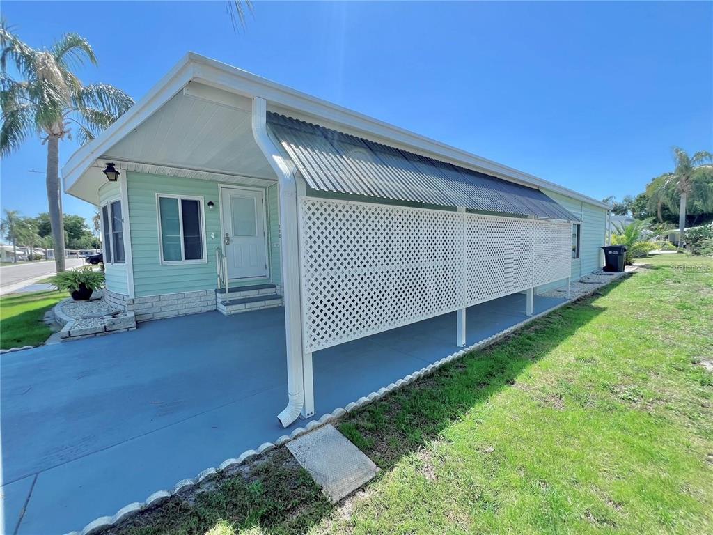 A light green mobile home features a covered carport with white lattice privacy screening — 1100 BELCHER ROAD S UNIT 772, LARGO, FL