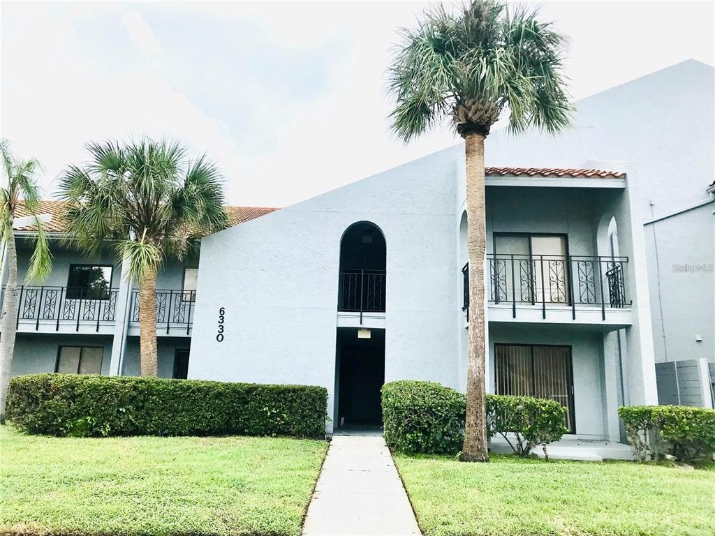 A two-story light blue apartment building features arched entryways, black metal railings, and palm trees — 6330 GRAND BAHAMA CIRCLE UNIT C, TAMPA, FL