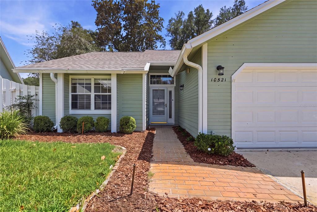 A light green house features a brick walkway leading to a front door and garage — 10521 NW 36TH PLACE, GAINESVILLE, FL