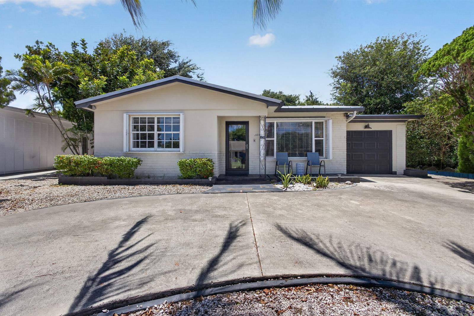 A single-story house with a beige exterior, a dark garage door, and a concrete driveway — 1964 Circle Drive, North Palm Beach FL 33408, NORTH PALM BEACH, FL