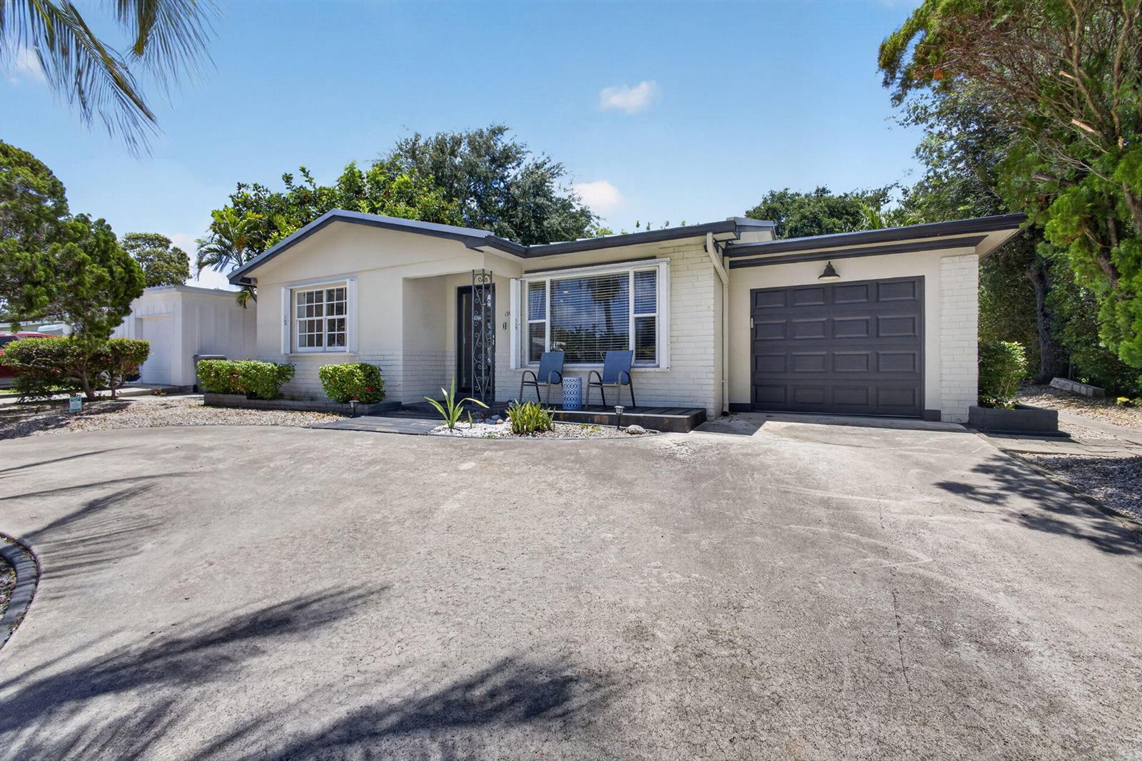 A single-story house with a white brick facade, dark garage door, and a concrete driveway — 1964 Circle Drive, North Palm Beach FL 33408, NORTH PALM BEACH, FL