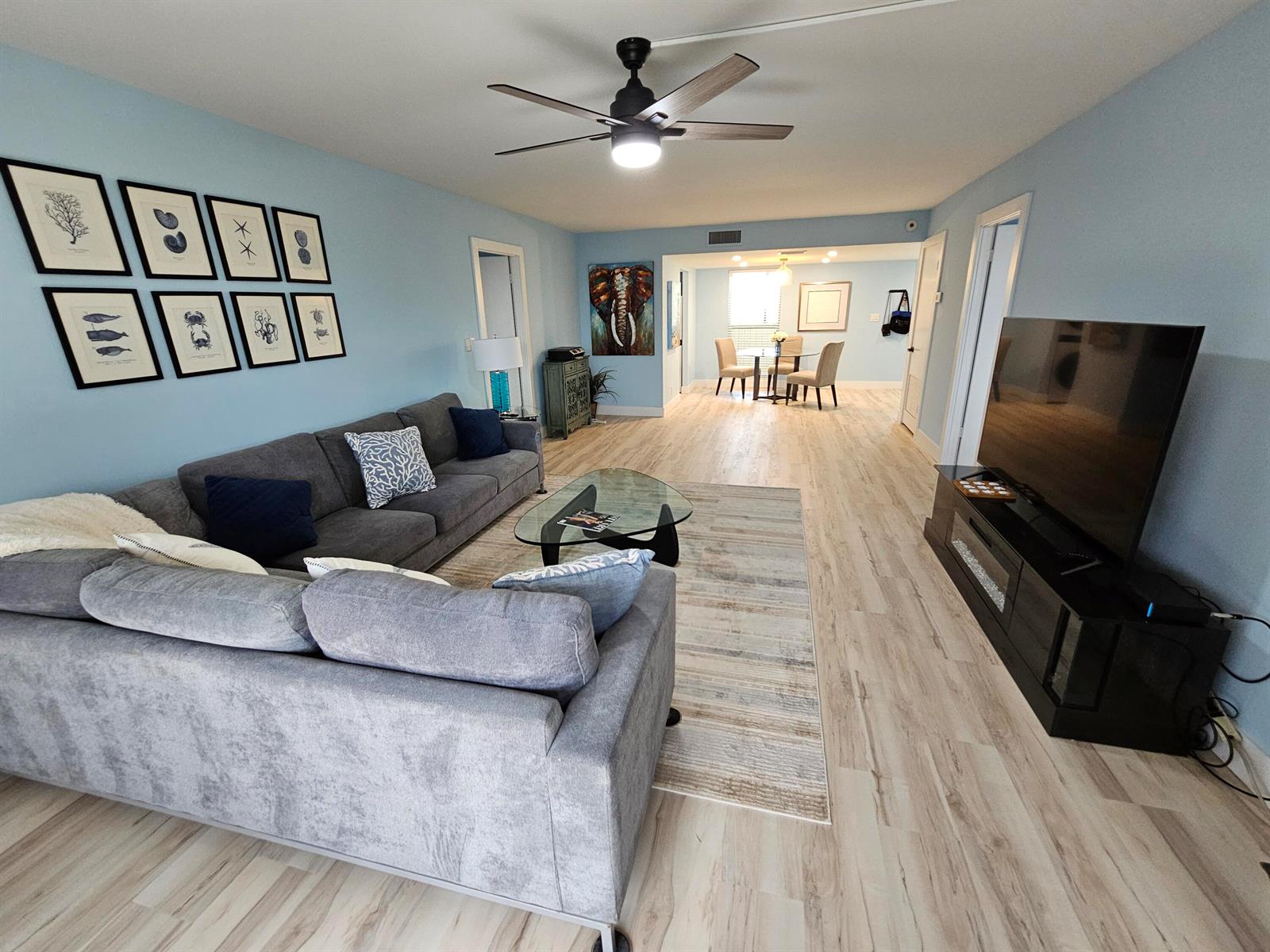 A living room with light blue walls, a gray sectional sofa, and light wood flooring — 1357 NE Ocean Boulevard # 312, Stuart FL 34996, STUART, FL